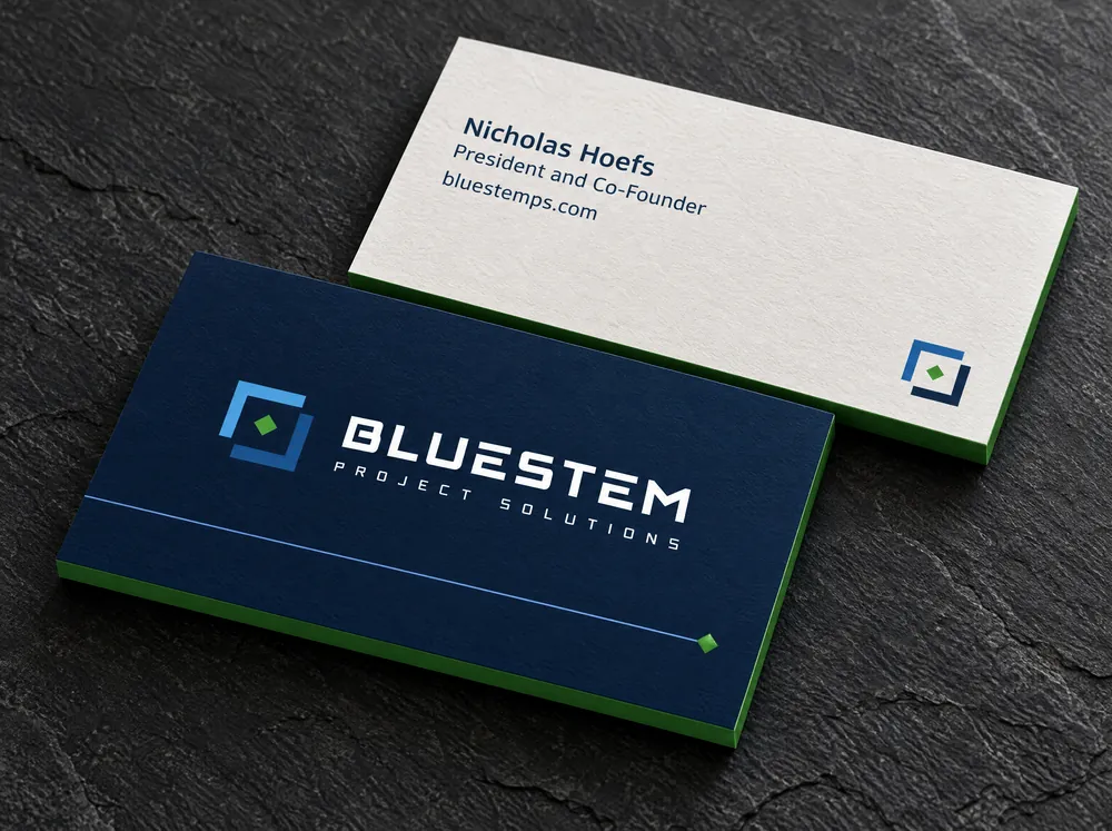 Two business cards on dark slate. The navy front carries the Bluestem logo above a thin blue line that ends in a green diamond, with a green edge. The white back shows the name Nicholas Hoefs, the title President and Co-Founder, the address bluestemps.com and the icon.
