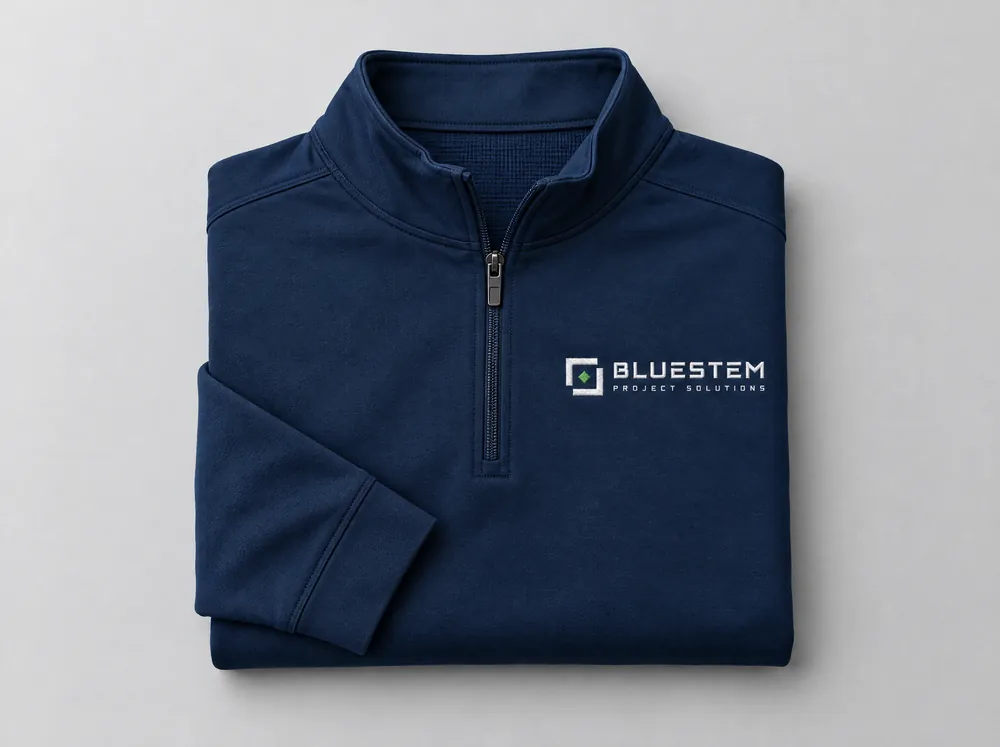 A folded navy quarter-zip pullover with a small white embroidered Bluestem logo and a green diamond on the left chest.